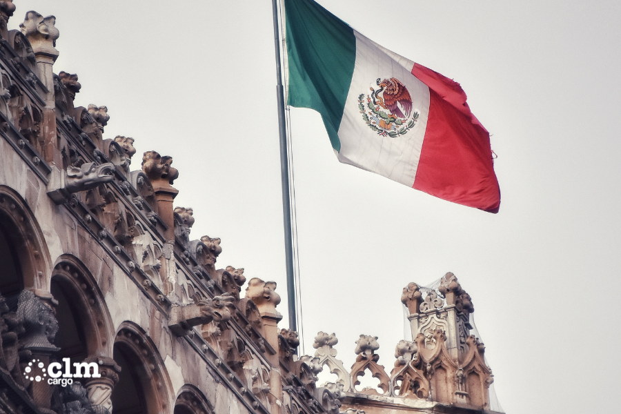 Una bandera Mexicana ondea en el viento frente a un edificio .
