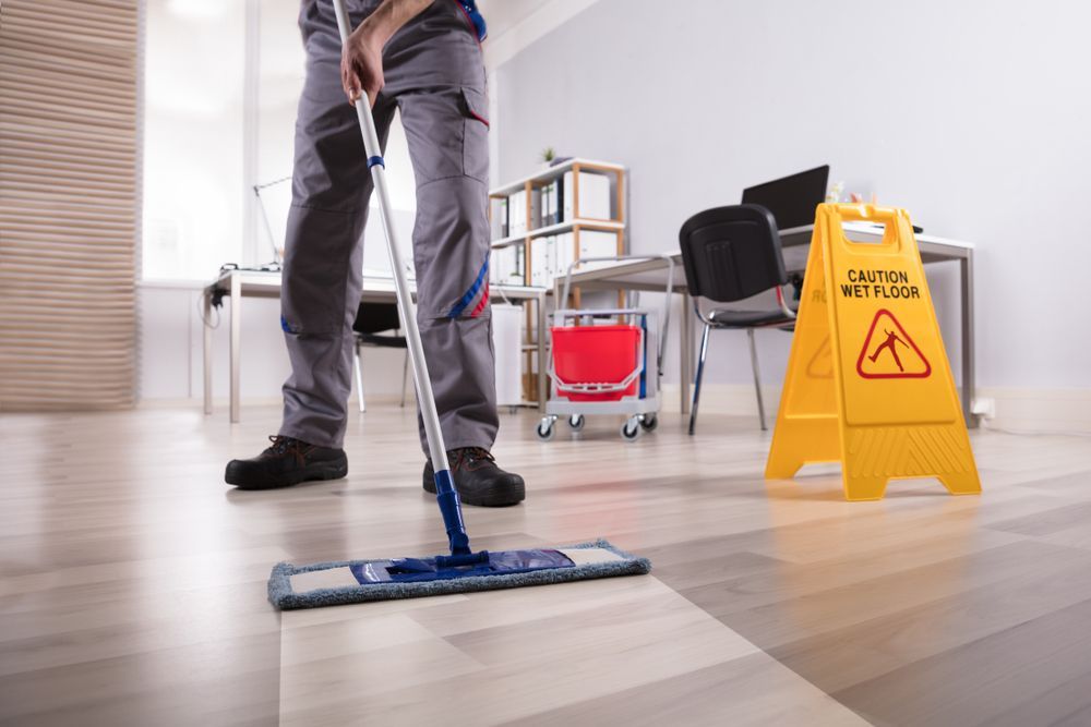 Person mopping an office floor beside a yellow wet floor sign and cleaning cart — A Plus Project Maintenance in Wodonga, VIC