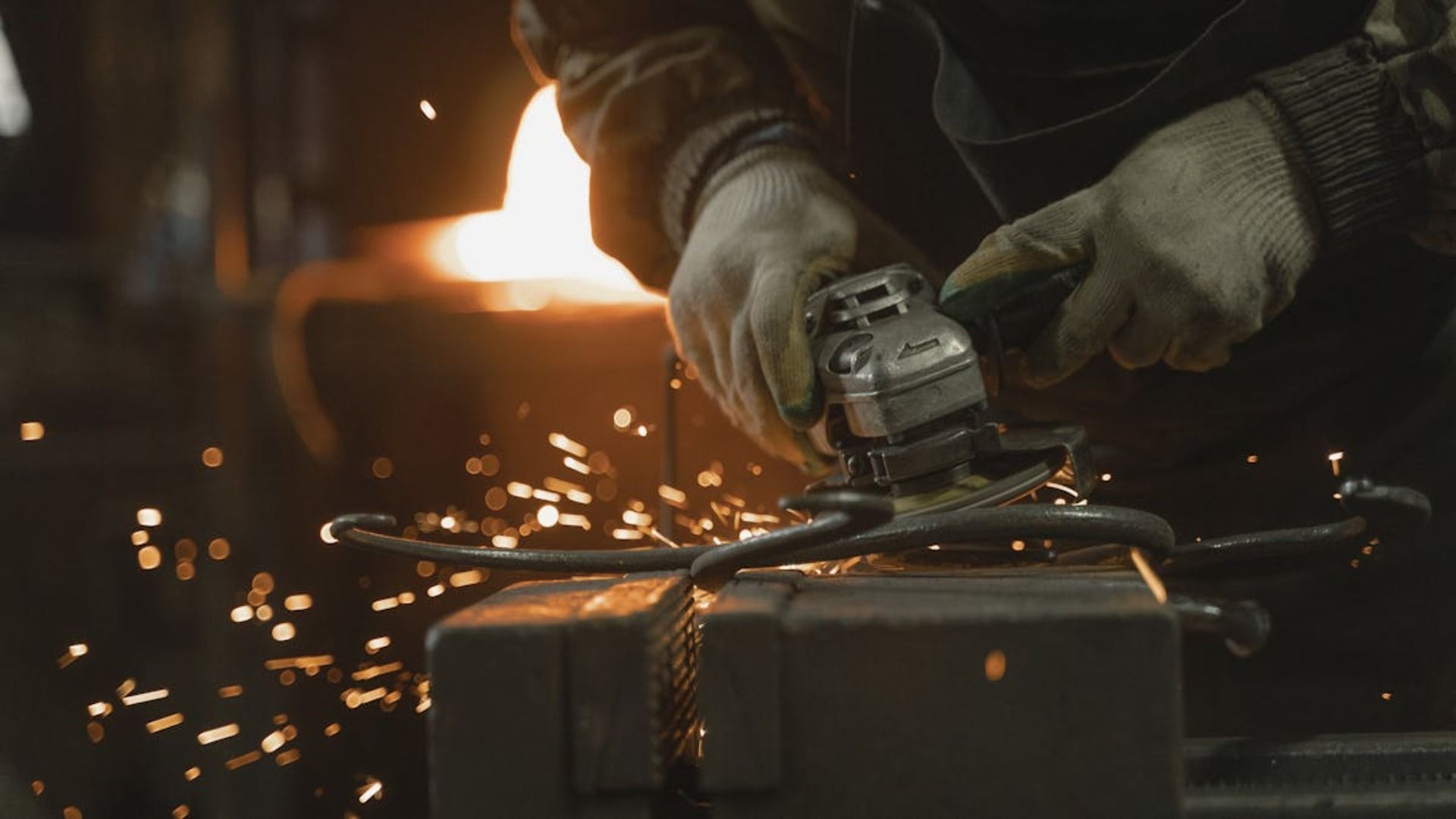Herrero utilizando una amoladora sobre un objeto de metal, saltan chispas y se produce una iluminación cálida.