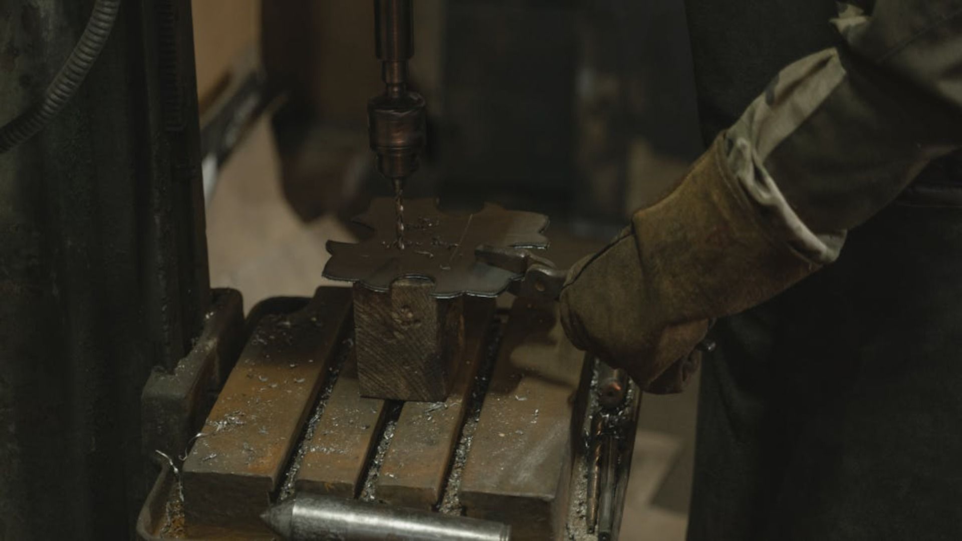 Una persona perfora un objeto metálico guardado en un taller, usando guantes protectores.