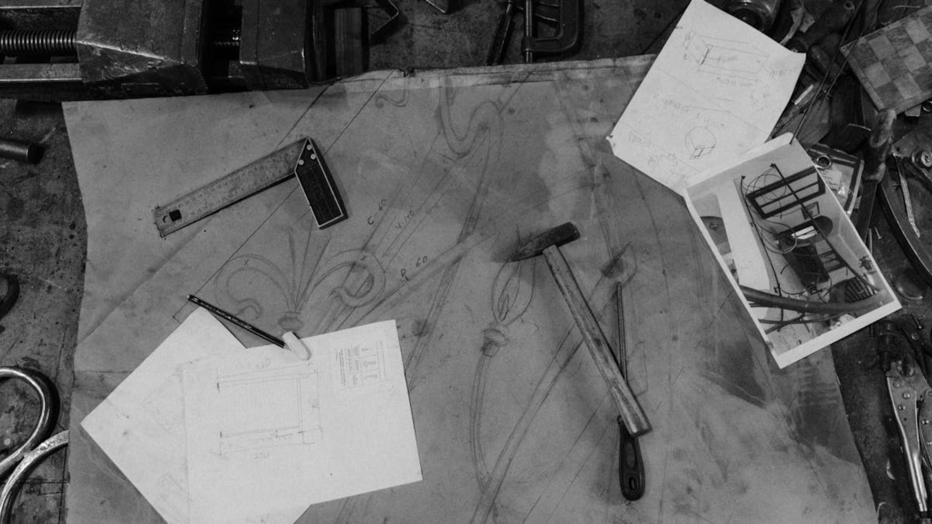 Mesa de taller con herramientas y bocetos, en blanco y negro.