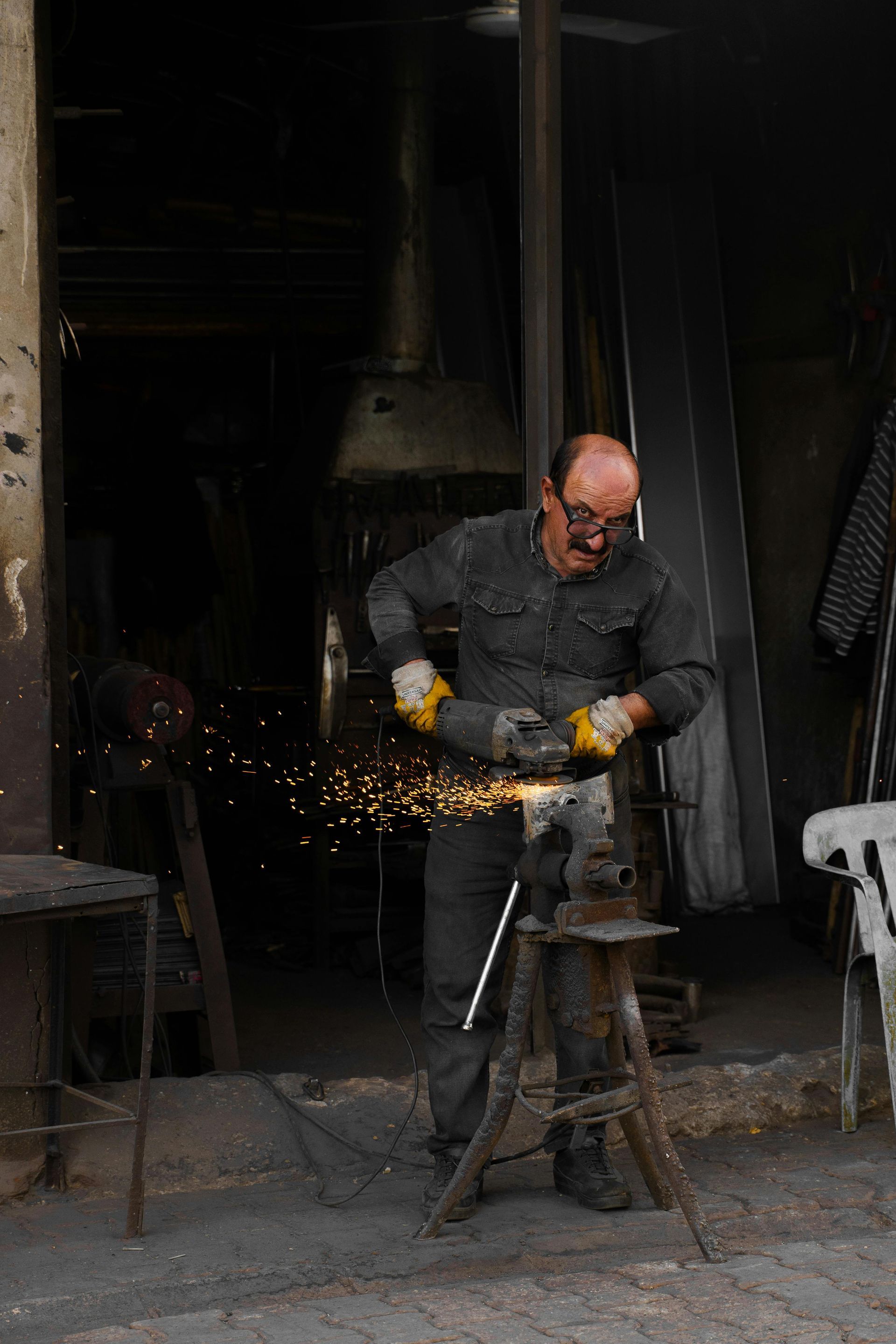 Un hombre con ropa de trabajo usa una amoladora, saltando chispas. Taller con metal.