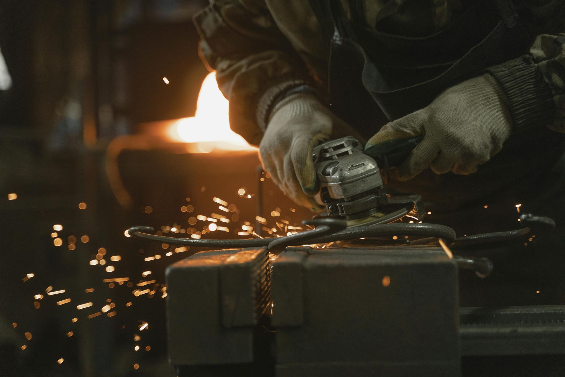 Herrero utilizando una amoladora sobre metal, saltando chispas, iluminado por una luz cálida en el taller.