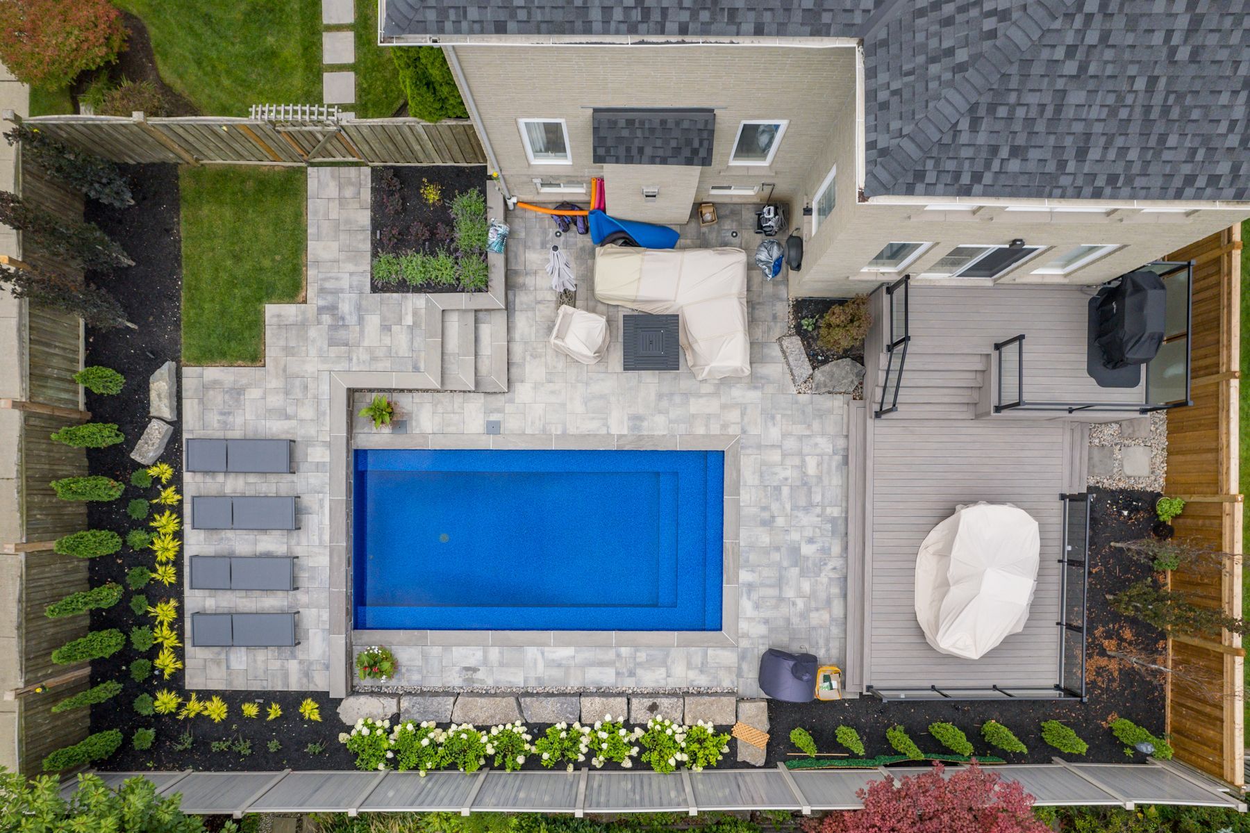 Aerial view of a backyard with pool, patio, and deck; gray stone and composite materials used.