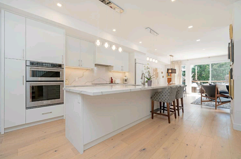 Modern white kitchen with island, light wood floors, and stainless steel appliances.