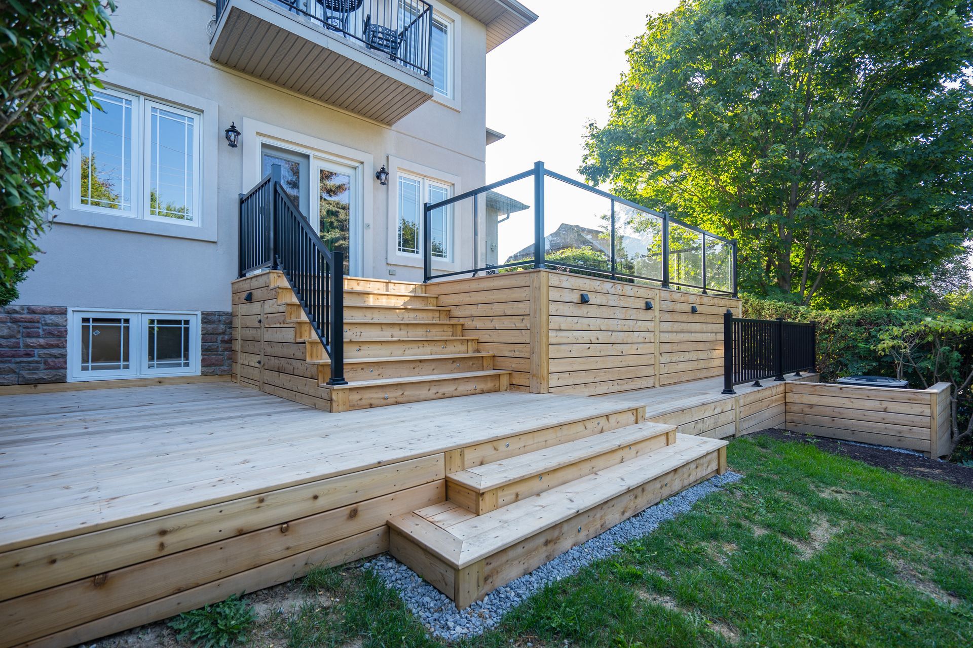 A wooden deck with stairs and a glass railing in the backyard of a house.