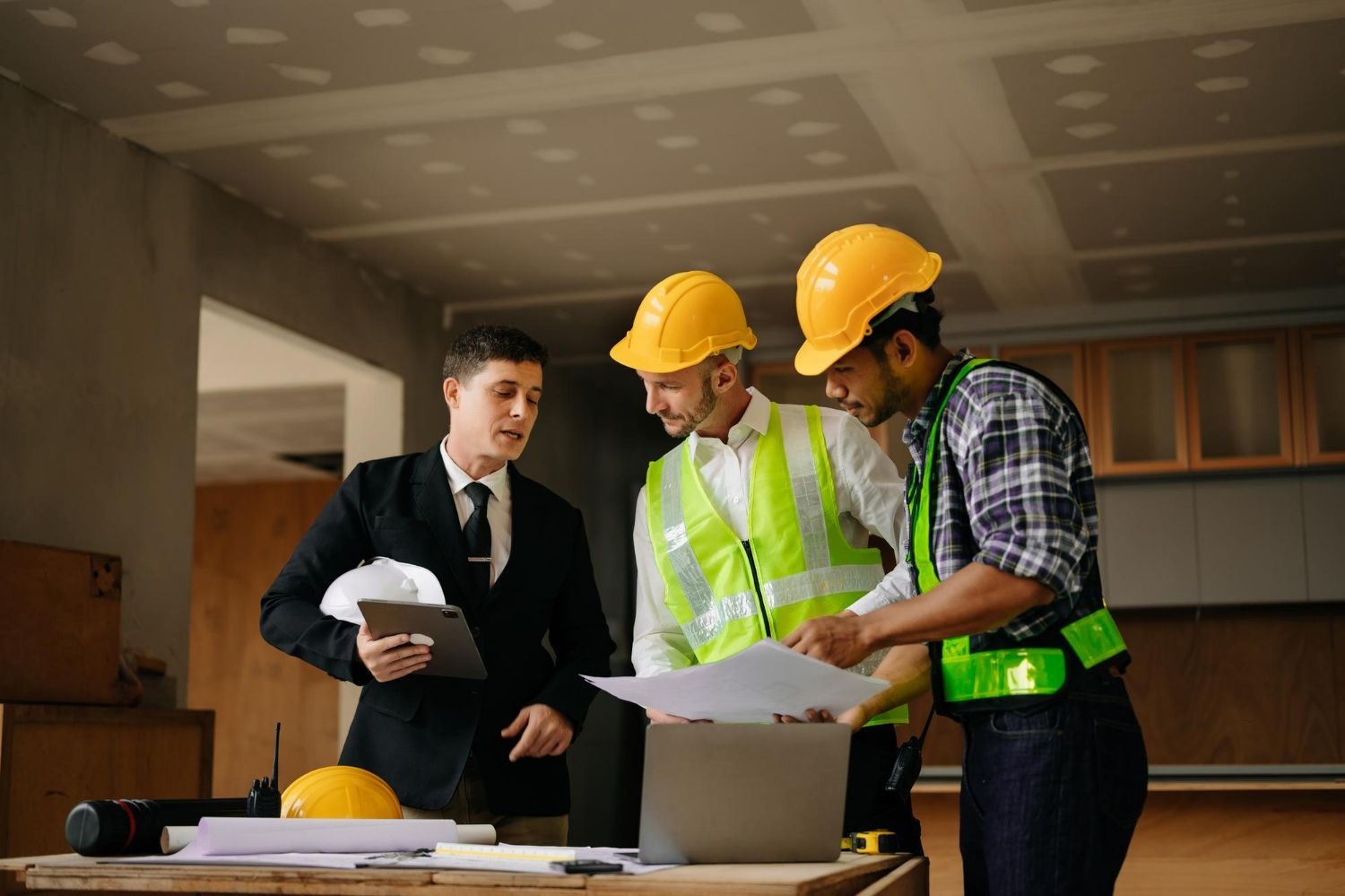 A group of construction workers are standing around a table looking at a laptop.
