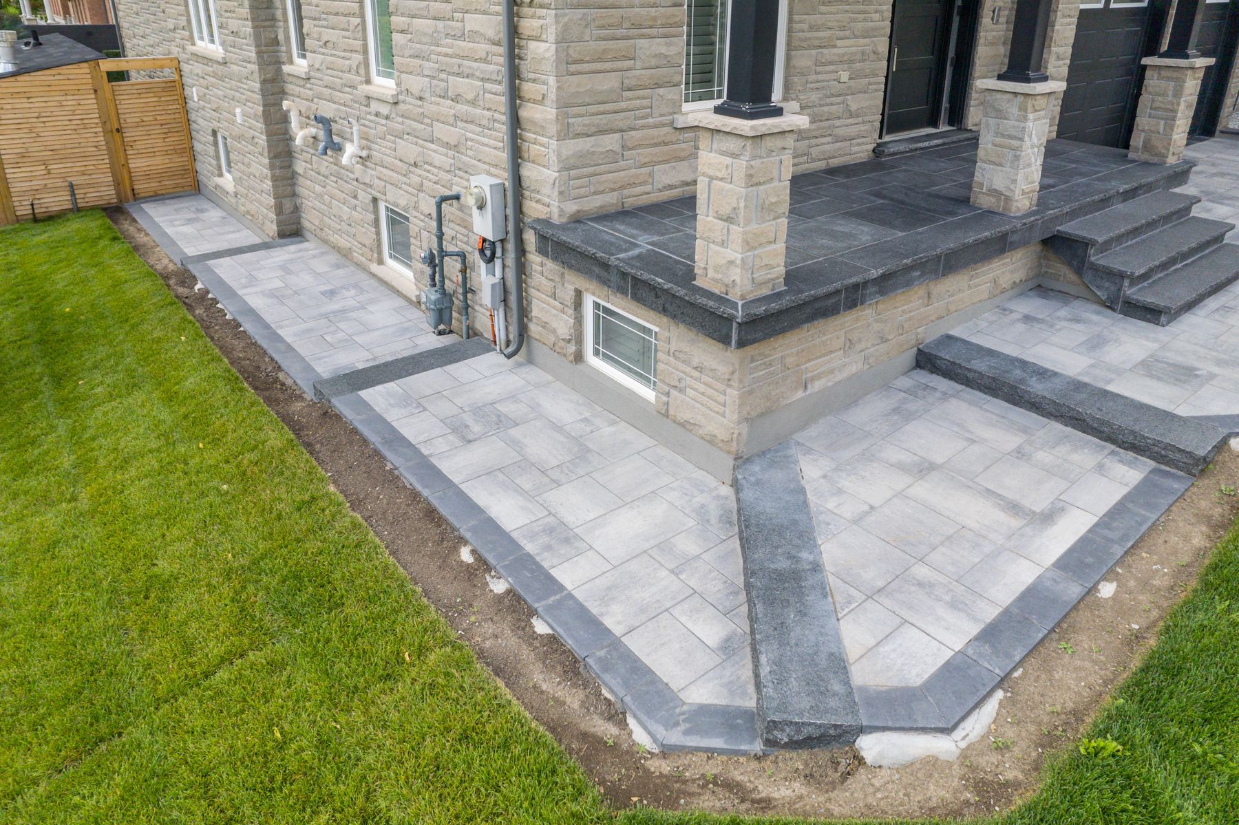 A house with a stone facade, a paved patio and walkway with dark edging.
