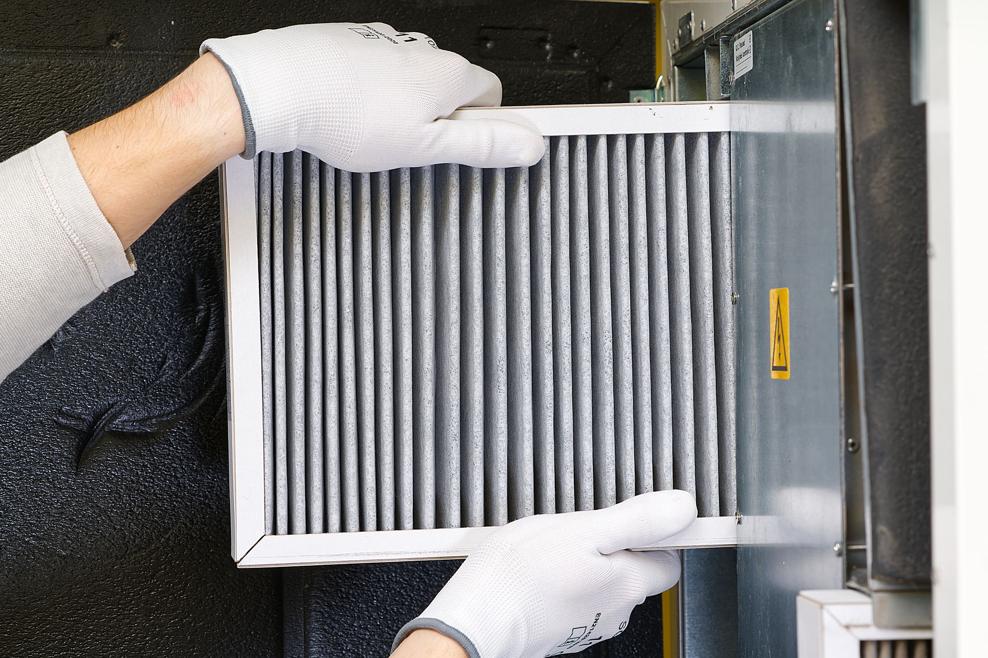 Hands in white gloves replacing an air filter; close-up shows pleated filter and metal frame.