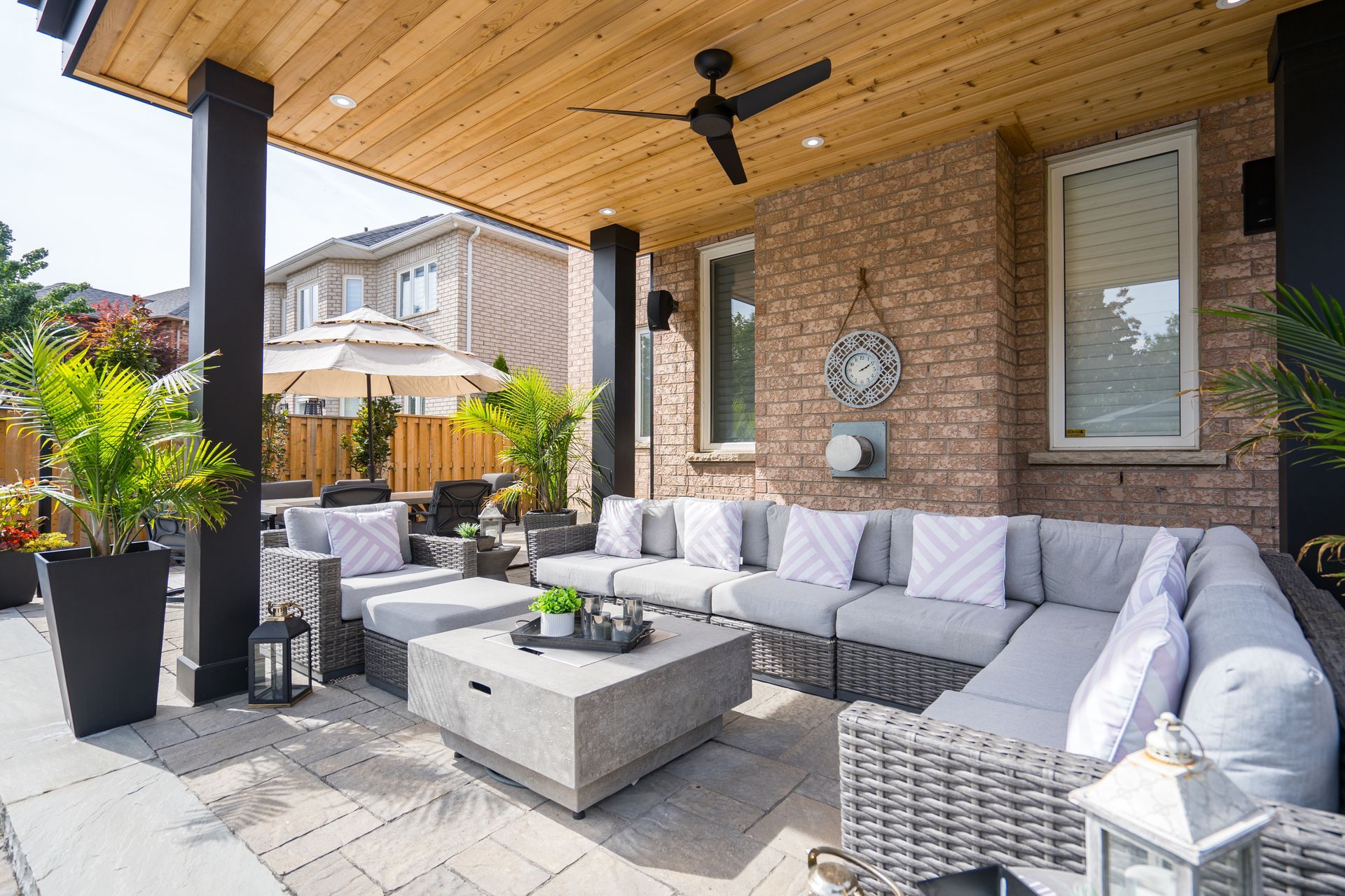 A patio with a sectional couch , chairs , a coffee table and a ceiling fan.