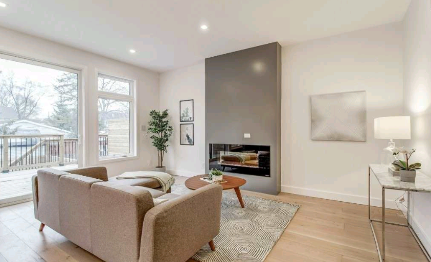 Modern living room with fireplace, beige sofa, large windows, and hardwood floors.