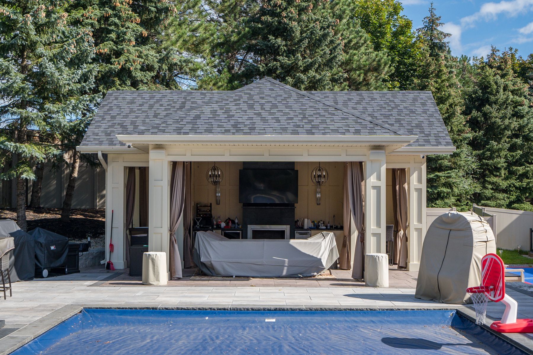 A gazebo with a television and a pool in the background.