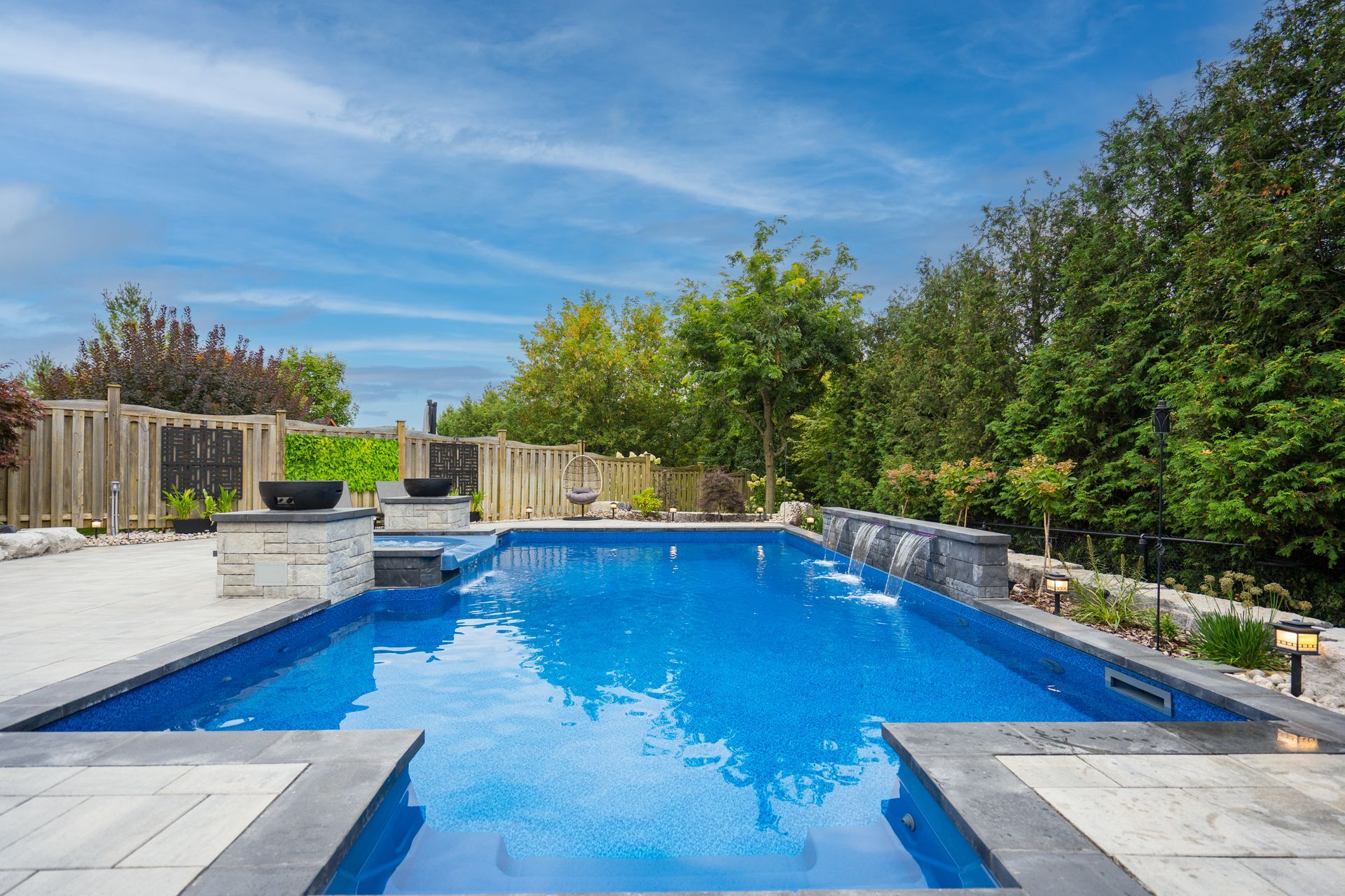 A large swimming pool in the backyard of a house surrounded by trees.