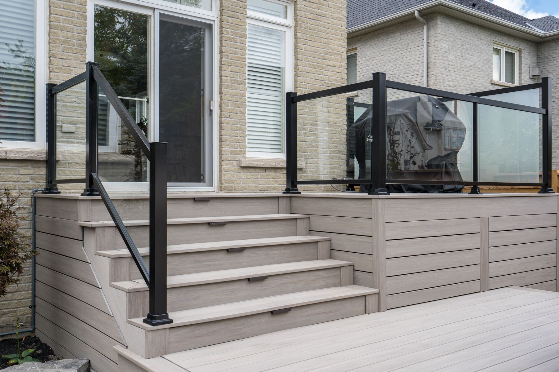 A deck with stairs and a grill on it in front of a house.