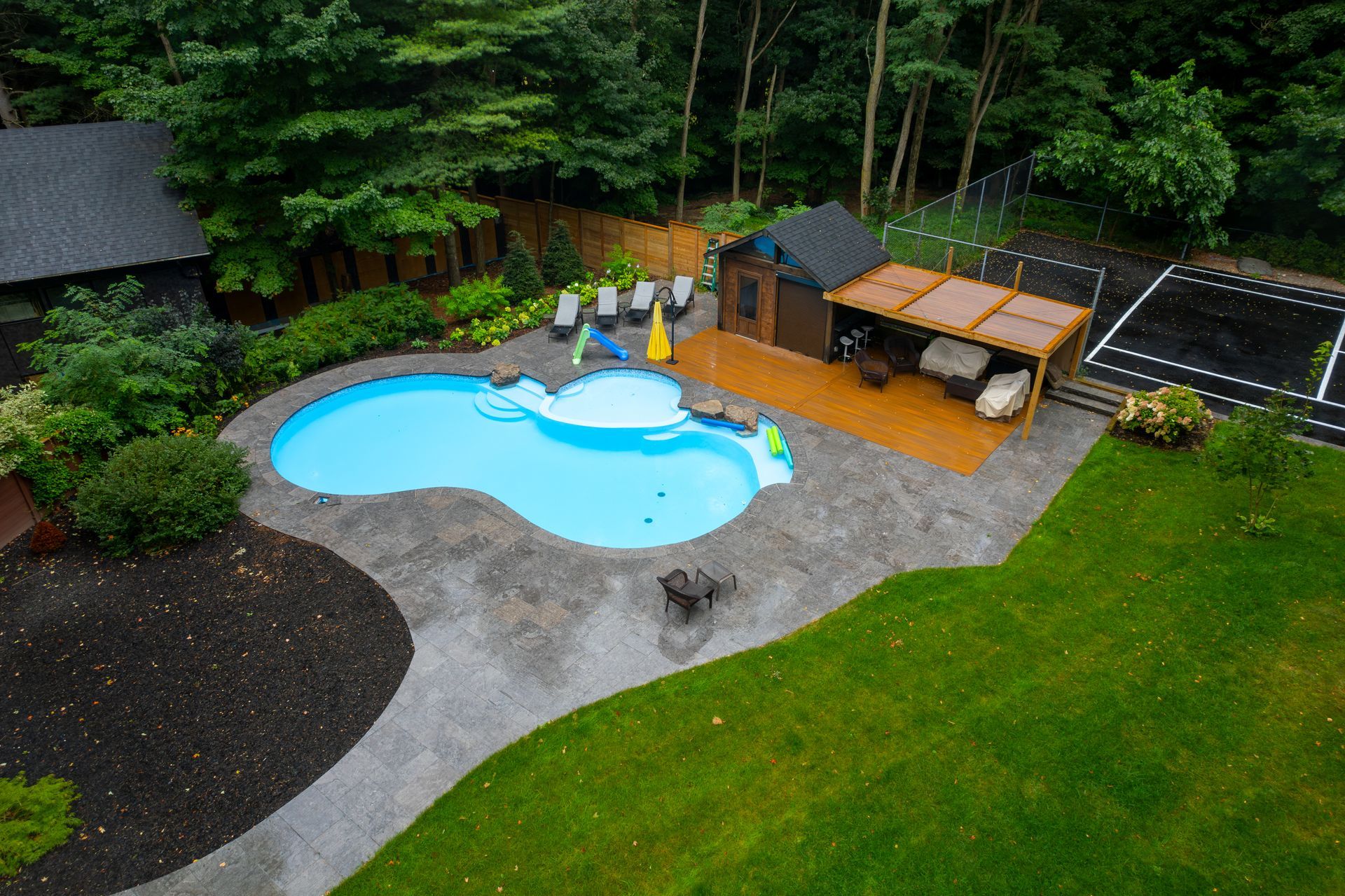 An aerial view of a backyard with a swimming pool and a tennis court.