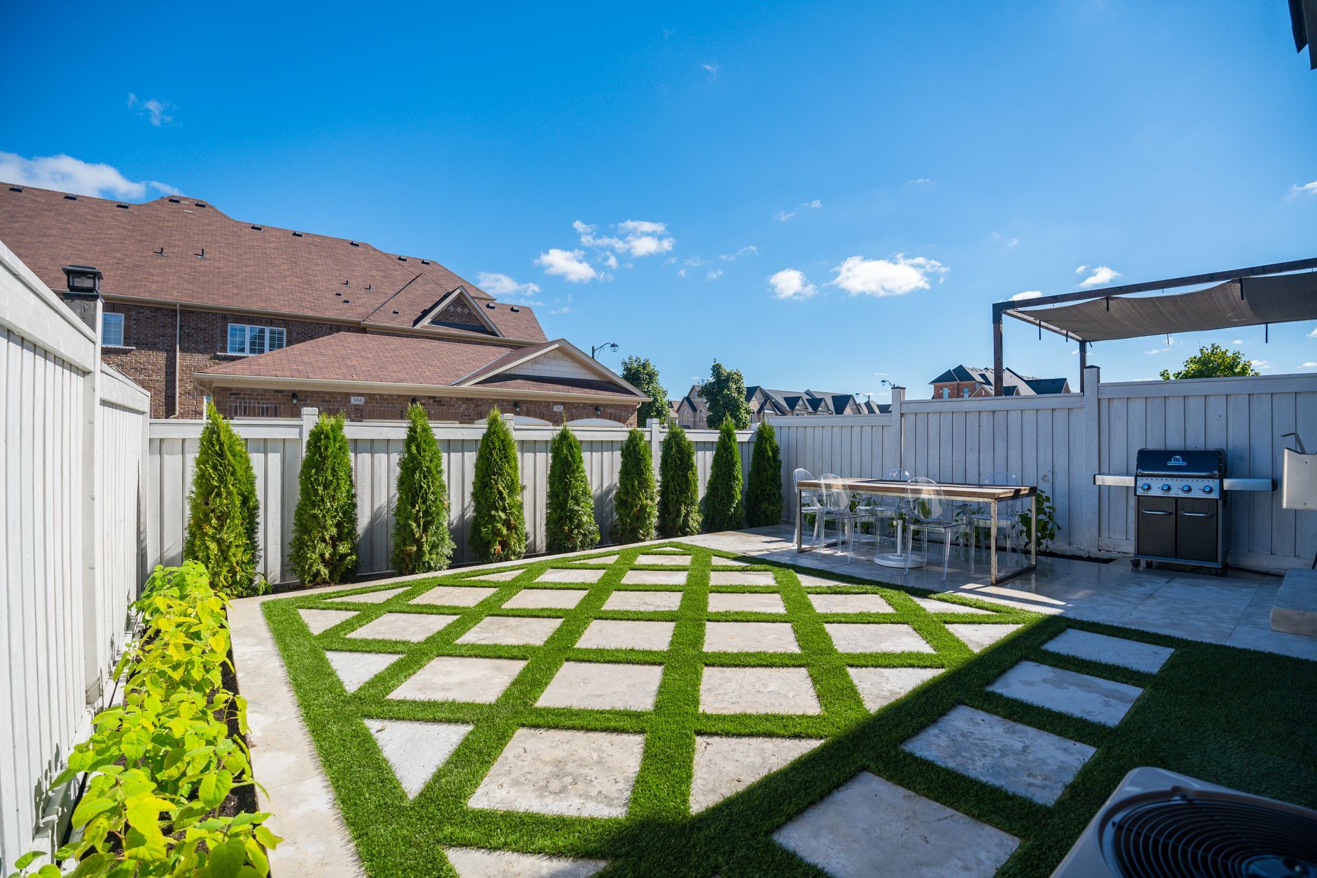 A backyard with a grill , table and chairs and a fence.