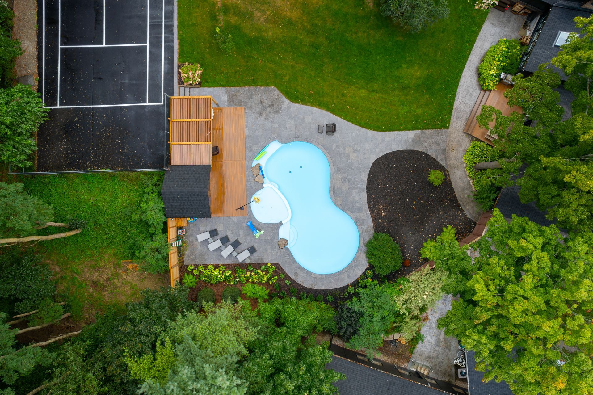 An aerial view of a backyard with a swimming pool and tennis court.