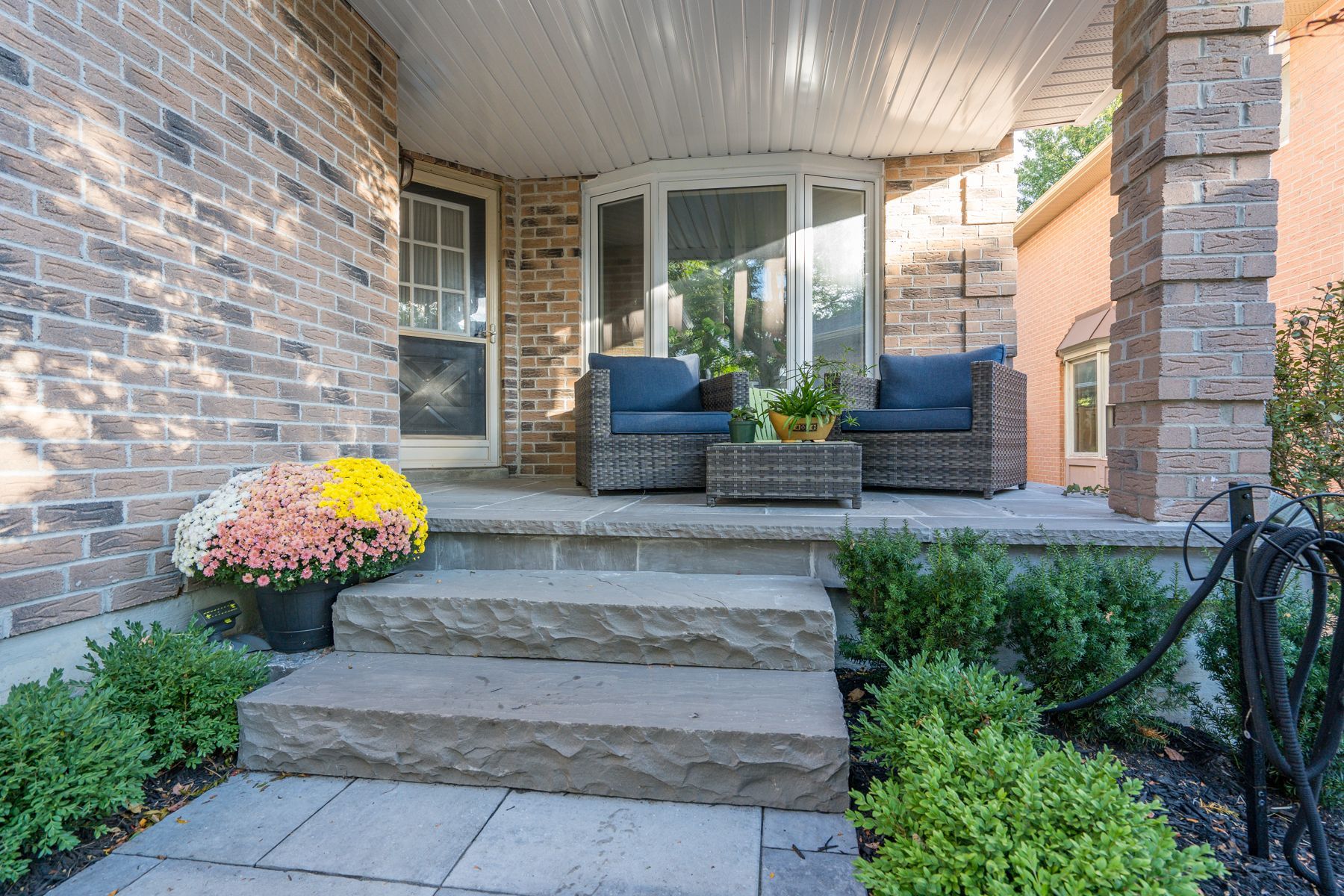 Brick home entrance with steps, seating, and potted flowers.