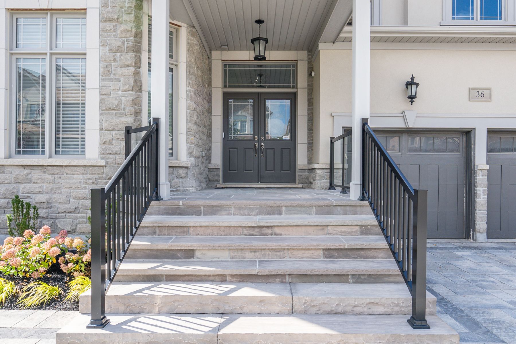 Gray stone steps lead up to a gray double-door entrance with black railings on a house with a stone and beige exterior.