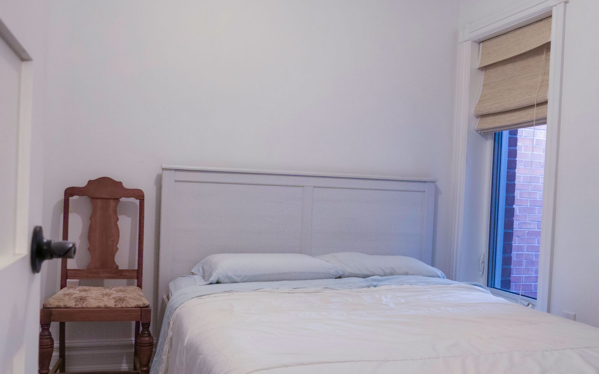 Bedroom with white walls, a bed with white bedding, and a patterned rug.