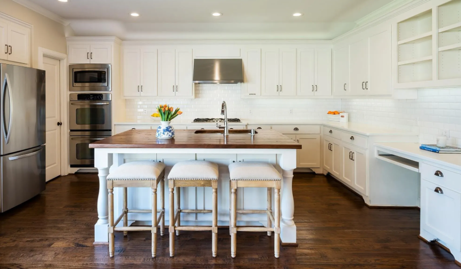 White kitchen with dark wood floors, island with stools, stainless steel appliances.