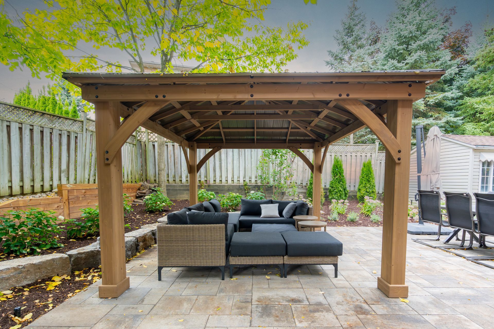 A wooden gazebo with a couch underneath it in a backyard.