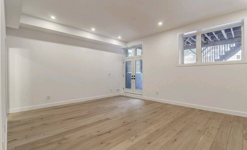 Empty room with hardwood floors, white walls, and natural light from a door and window.