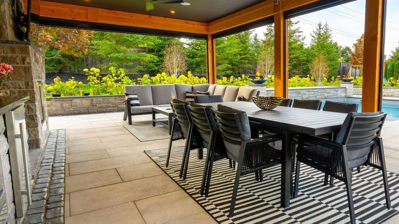 Covered outdoor patio with dining table, sofa, and pool in the background; green trees frame the view - MSD Contracting GTA