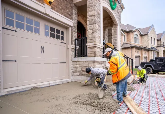 Construction workers pouring and smoothing concrete for a front walkway near a garage.