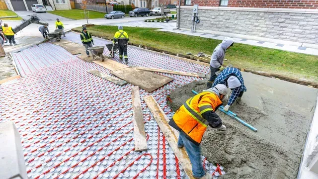 Construction workers laying concrete on a sidewalk with embedded heating system, outdoors.