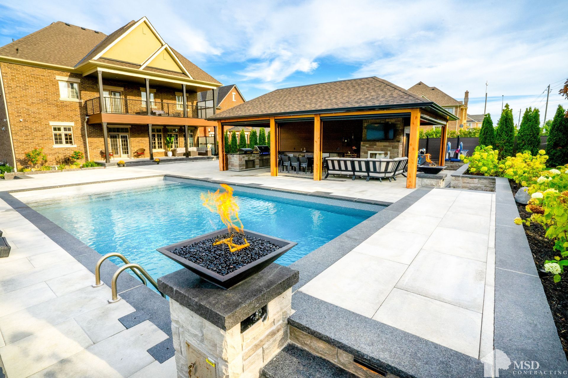 A large swimming pool with a fire pit in front of a house.