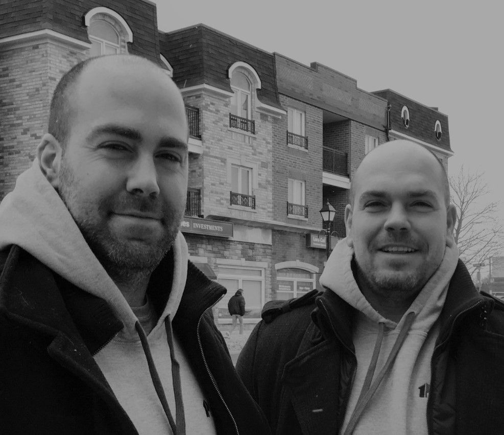 Two bald men are standing next to each other in front of a building.