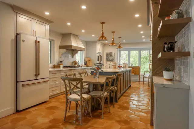 Cozy kitchen with light cabinets, copper pendant lights, island with dining area, and orange-tiled floor.