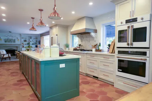Modern kitchen with teal island, copper pendant lights, and red-toned hexagonal tile flooring.