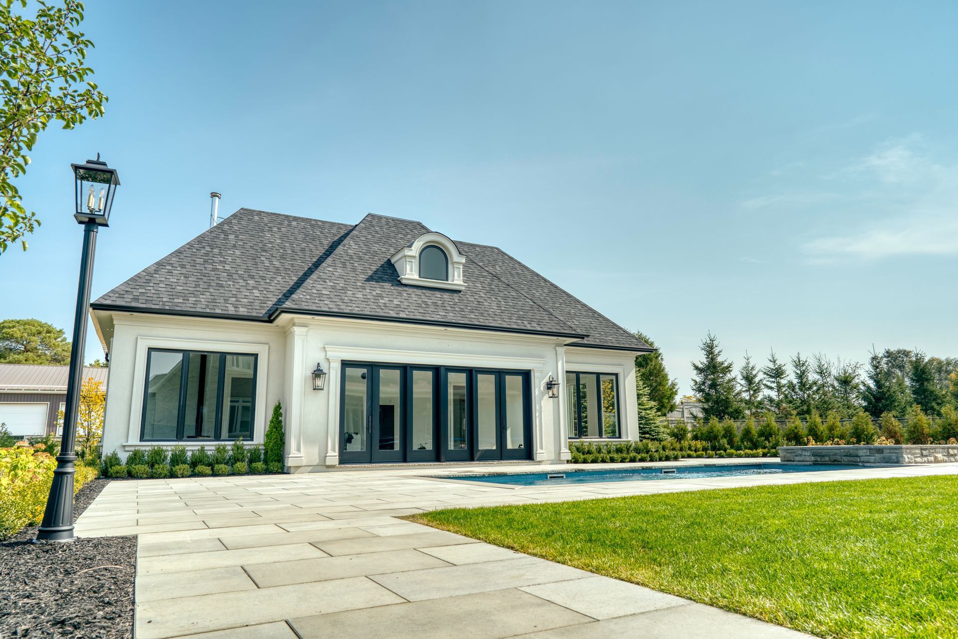 A white house with a black roof and a swimming pool in front of it.