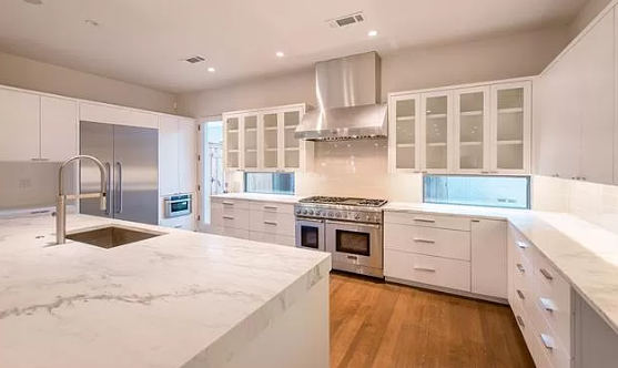 A kitchen with white cabinets , stainless steel appliances , a sink , and a large island.