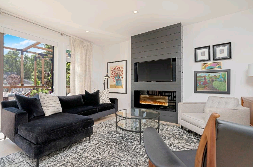A living room with a black couch , white chairs , a fireplace and a flat screen tv.
