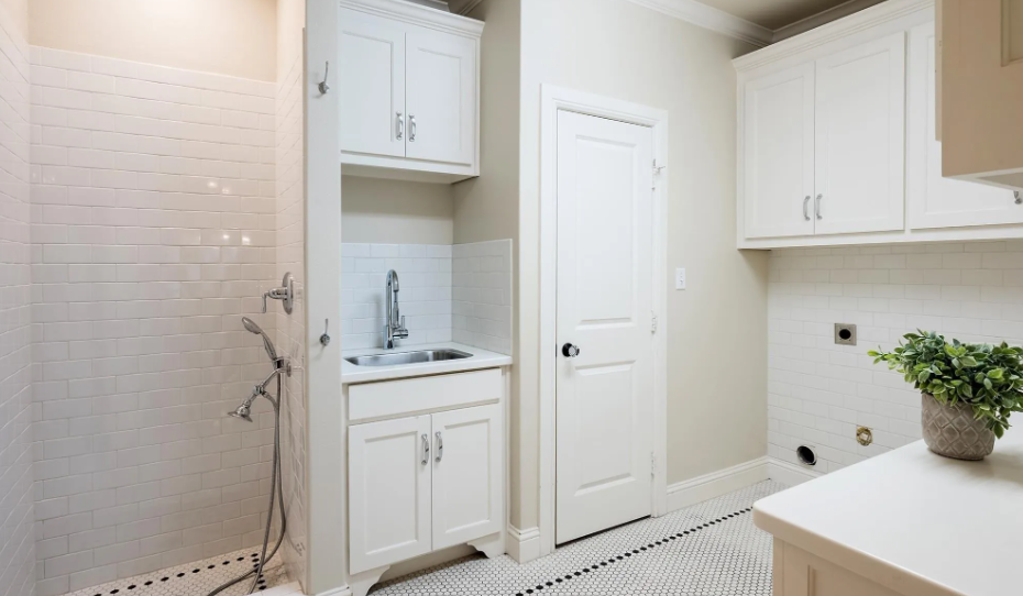A laundry room with a sink , cabinets , and a walk in shower.