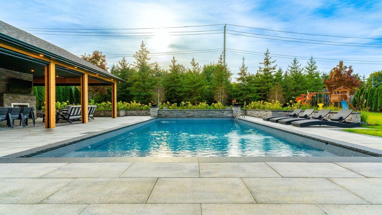 MSD Contracting Completed Landscape Construction - Pool with patio and lounge chairs, surrounded by trees and a sunny sky.