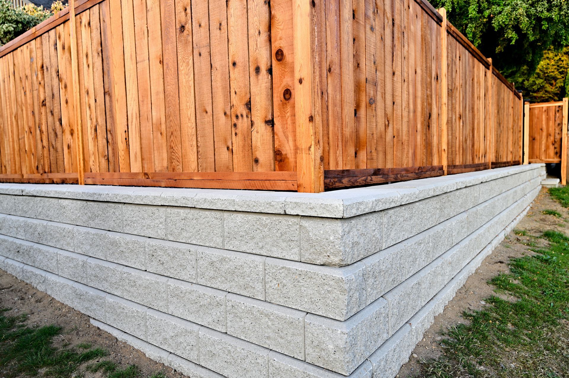Wooden fence atop a light gray block retaining wall in a yard, with grass in front.