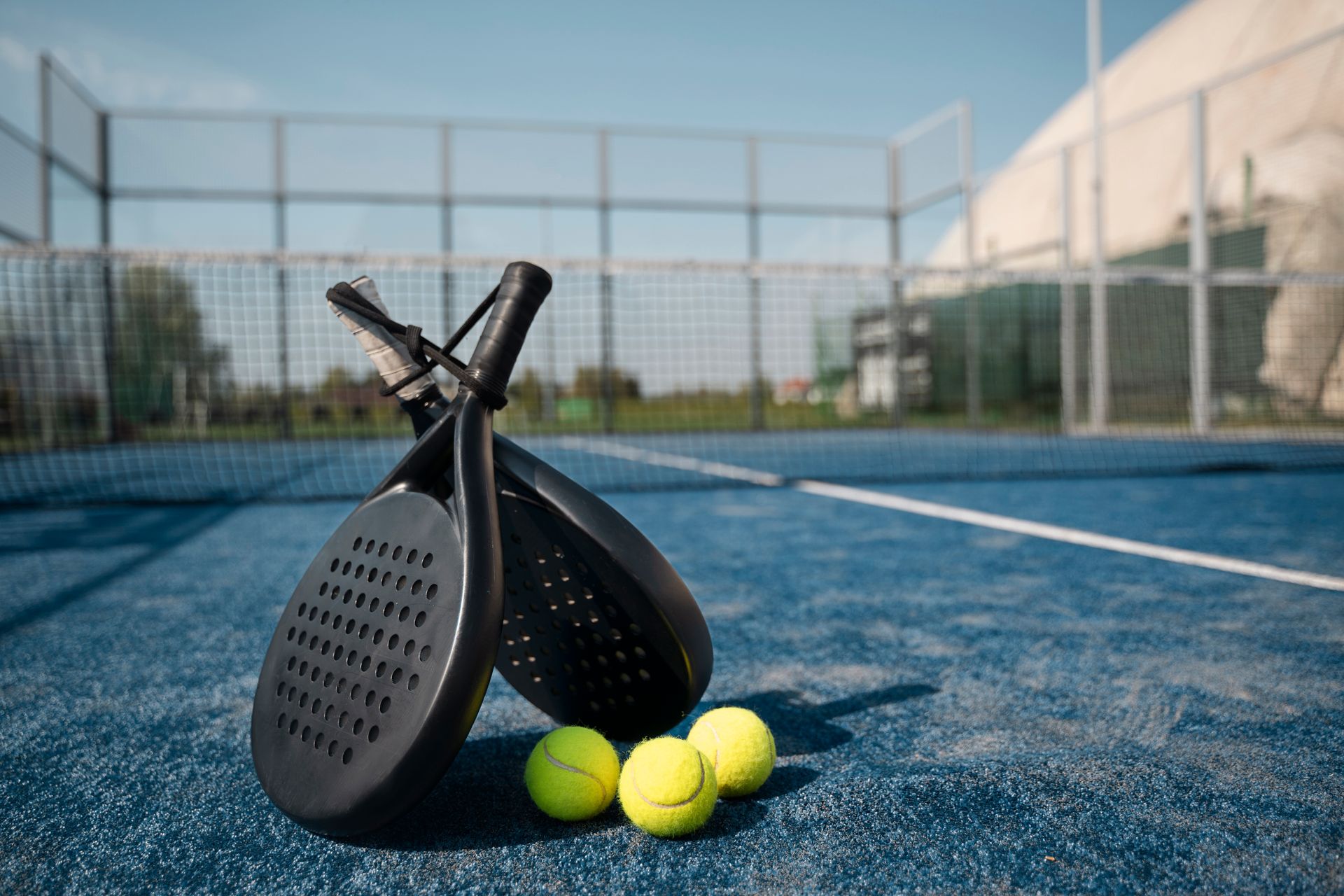 A pair of paddle tennis rackets and three tennis balls on a tennis court.
