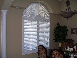 A living room with a large arched window with shutters on it.