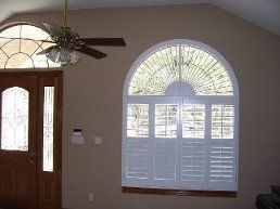 A living room with a large arched window and a ceiling fan.