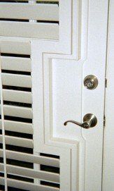 A close up of a white door with shutters and a door handle.