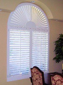 A dining room with a large arched window with shutters on it.