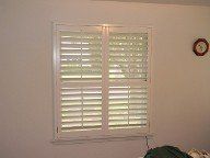 A bedroom window with white shutters and a clock on the wall.