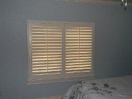 A bedroom with a bed and a window with shutters on it.