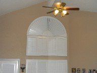 A ceiling fan is hanging from the ceiling above a window with arched shutters.