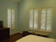 A bedroom with a bed , dresser , television and shutters on the windows.
