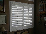 A living room with a window with white shutters on it.